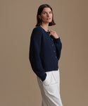 Woman wearing a navy cardigan and white pants against a beige background