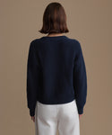 Person wearing a navy sweater and white pants against a beige background