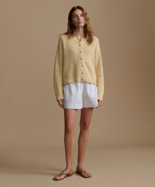 Woman wearing a yellow cardigan and stripe shorts on a beige background