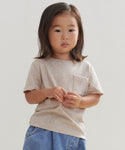 A young child with medium-length dark hair stands against a plain light background, wearing the Kids Vintage Pocket Tee in 100% cotton, paired with blue denim shorts and looking forward with a neutral expression.