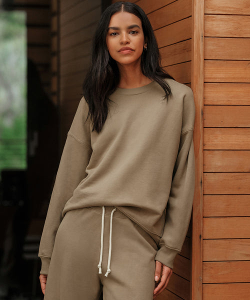 A woman with long dark hair wears the Marina Sweatshirt, standing against a wooden wall and looking at the camera with a neutral expression—a cozy loungewear look.