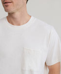 A man wears the Mens Vintage Pocket Tee in ivory, relaxed fit, with a chest pocket. Shown from shoulders to mid-torso against a neutral background, his face is partially visible.