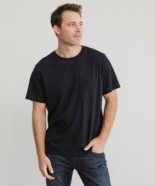 A man wearing the Mens Vintage Pocket Tee and blue jeans stands against a light grey background, looking slightly to his left with one hand in his pocket.