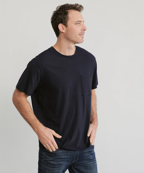 A man wearing the Mens Vintage Pocket Tee and blue jeans stands with his hands in his pockets, looking off to the side against a light gray background.