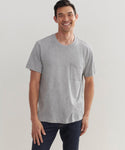 A smiling man stands against a plain light background, wearing the Mens Vintage Pocket Tee in grey with a chest pocket, paired with dark jeans.