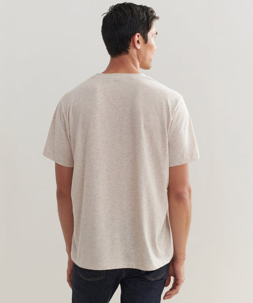 A man with short dark hair stands with his back to the camera, wearing the Mens Vintage Pocket Tee in light beige and dark jeans against a plain light background.