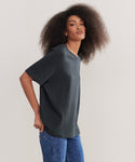 A person with voluminous curly hair wears a black Relaxed Tee and blue jeans, standing against a plain light background.