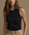 Woman wearing a black sleeveless top and beige pants against a neutral background