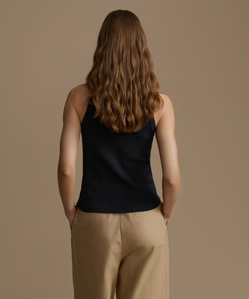 Person wearing a black sleeveless top and beige pants against a brown background