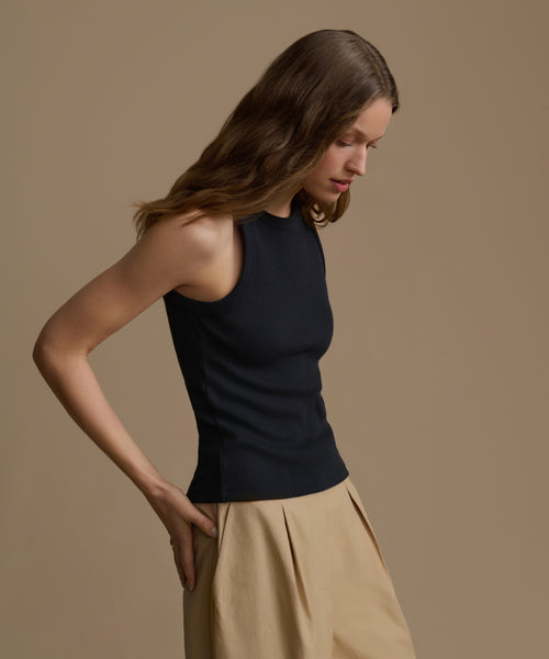 Woman wearing a black sleeveless top and beige pants against a brown background