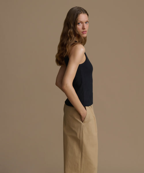 Woman wearing a black sleeveless top and beige pants against a brown background