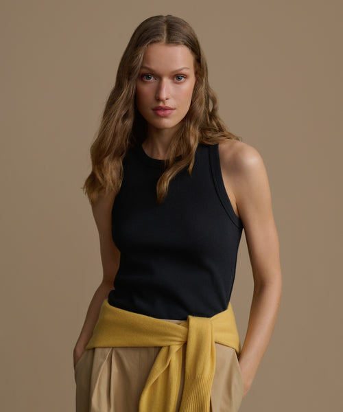 Woman wearing a black sleeveless top and yellow and beige skirt against a brown background
