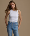 Woman wearing a white tank top and blue jeans against a beige background