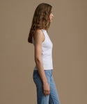 Woman wearing a white tank top and blue jeans against a brown background