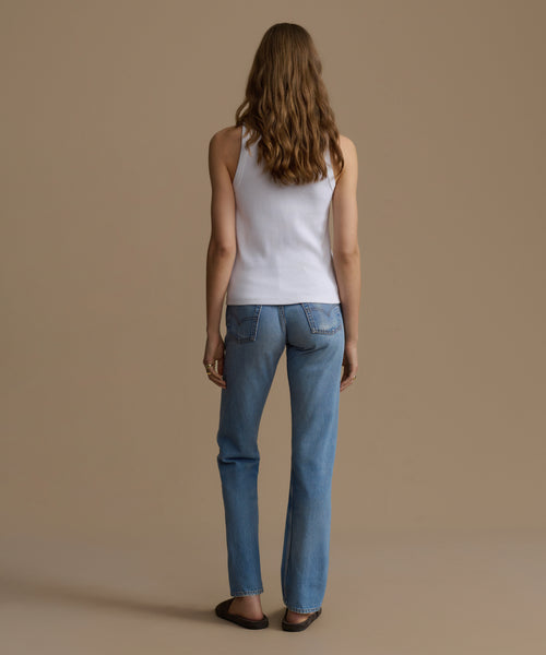 Person wearing a white tank top and blue jeans on a beige background