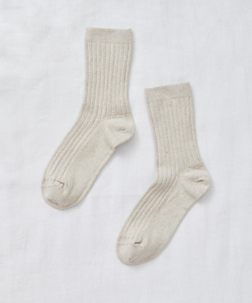 A pair of light beige Rib Socks, perfect for all seasons, is laid flat on a white fabric background with the toes facing opposite directions.