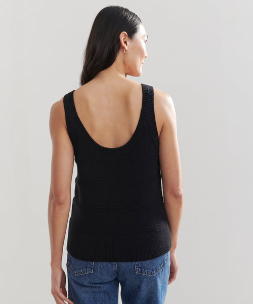A woman with long dark hair is shown from the back, wearing a black Sweater Tank and blue jeans against a plain light background.