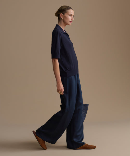 Woman wearing a dark navy courtney top and navy outfit against a beige background