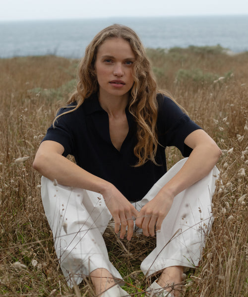 Woman sitting in a field with ocean in the background wearing a dark navy courtney top