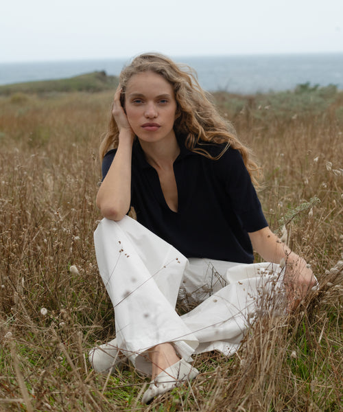 Woman sitting in a field with ocean view wearing a dark navy courtney top