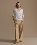 Woman wearing a ivory courtney top and beige pants against a beige background