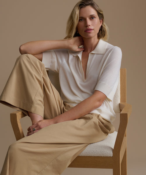 Woman sitting on a chair wearing a ivory courtney top and beige pants against a beige background