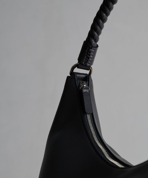 Close-up of the Crescent Shoulder Bag, crafted from soft leather in Italy, with a silver zipper and braided handle, shown against a plain light gray background.