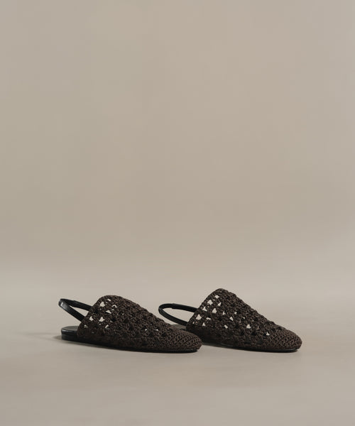 The Crochet Jules Mule slip-on sandals feature a black crochet design with a closed toe, open heel, and are displayed on a neutral beige background.