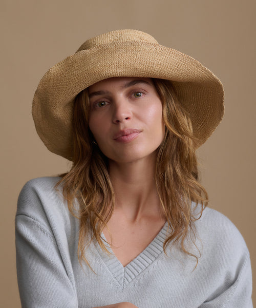 Woman wearing a beige straw hat against a beige background