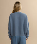 A person with long blonde hair, seen from behind, wears a light blue Cropped Cashmere Cocoon Cardigan and matching pants, standing against a plain beige background.