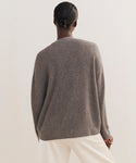 Seen from behind against a plain, light background, a person with dark hair in a low bun wears the Cropped Cashmere Cocoon Cardigan in gray with white pants.