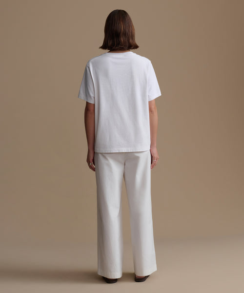 Person wearing a white t-shirt and pants on a beige background