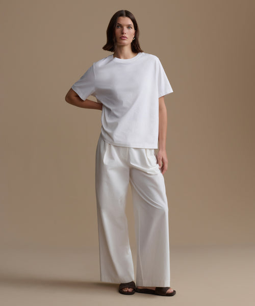 Person wearing a white t-shirt and pants on a beige background