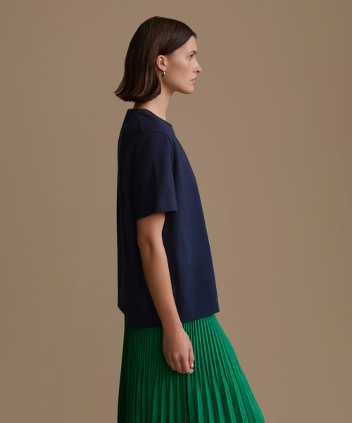 Woman wearing a navy blue top and green pleated skirt on a beige background