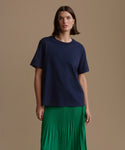 Woman wearing a navy blue top and green pleated skirt on a brown background