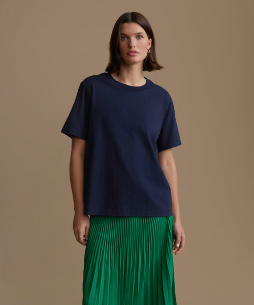 Woman wearing a navy blue top and green pleated skirt on a brown background