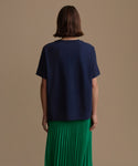 Woman wearing a navy blue top and green pleated skirt on a beige background