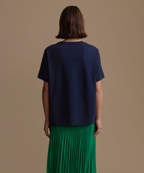 Woman wearing a navy blue top and green pleated skirt on a beige background