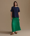 Woman wearing a navy top and green pleated skirt on a beige background