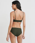 A woman with long dark hair is seen from the back against a plain background, wearing the Cruz Bay Bikini Bottom in olive green, made from recycled nylon with a high-cut fit and matching adjustable-strap bikini top.