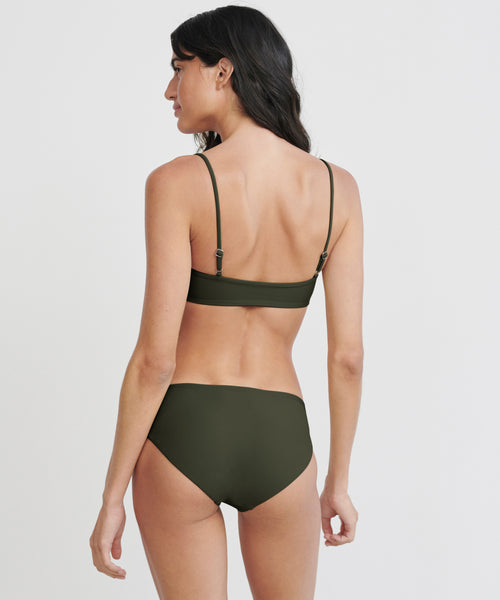 A woman with long dark hair is seen from the back against a plain background, wearing the Cruz Bay Bikini Bottom in olive green, made from recycled nylon with a high-cut fit and matching adjustable-strap bikini top.