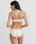 A woman with long dark hair is seen from behind, wearing the Cruz Bay Bikini Bottom in white, set against a plain light background.