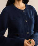 A woman with long dark hair and a green ring wears the Charlotte Cardigan in navy, featuring front pockets. She holds her hands together, showcasing the stylish upper-body look of this womens cardigan.
