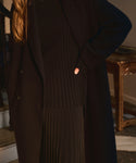 A person with long light brown hair stands indoors, one hand on their hip, wearing the Dara Top and a black coat. Their face is not visible.