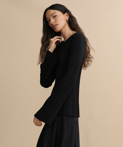 Woman with long, wavy dark hair wears the Dara Top and a black skirt, standing against a beige background and looking at the camera with a relaxed expression.