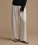 Person wearing beige wide-leg pants and black sandals on a beige background