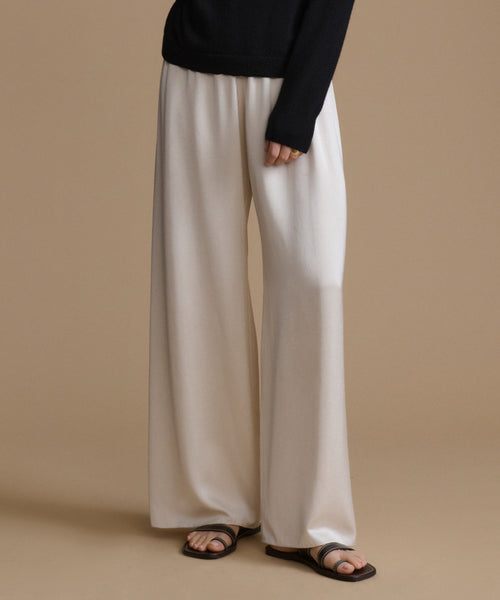 Person wearing beige wide-leg pants and black sandals on a beige background