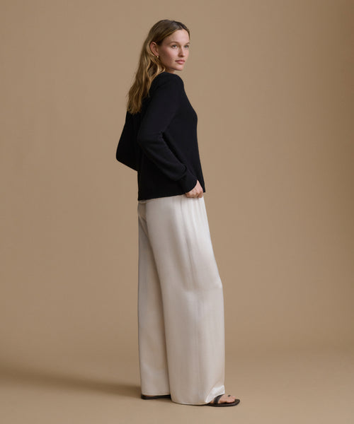 Woman wearing a black top and white pants against a beige background