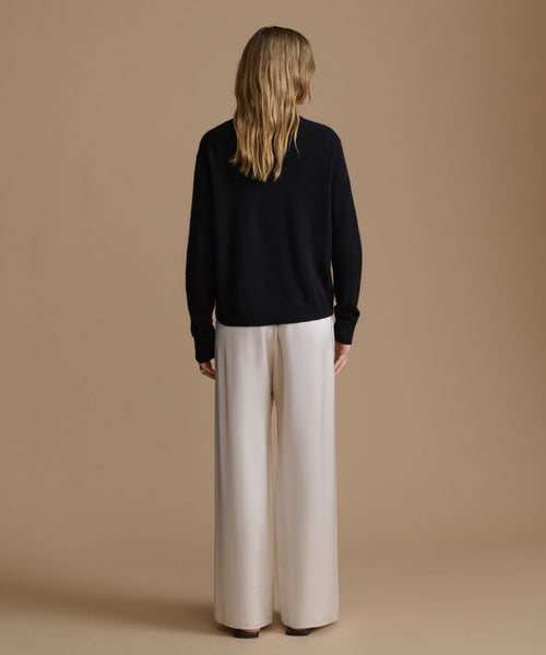 Woman wearing a black sweater and beige pants against a brown background