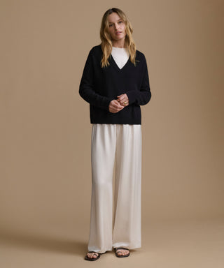Woman wearing a black sweater and white pants against a beige background